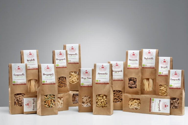 Verschiedene italienische Pasta Marken in braunen Verpackungen, einzeln verpackt, auf weißem Tisch, hinter grauem Hintergrund.