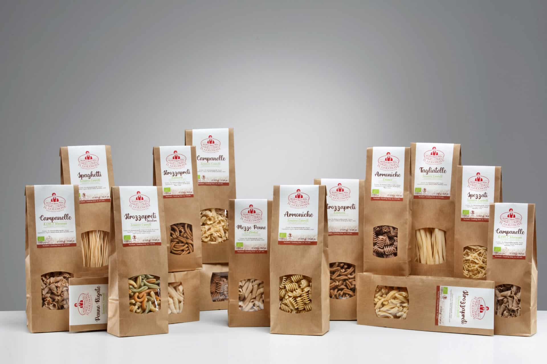 Verschiedene italienische Pasta Marken in braunen Verpackungen, einzeln verpackt, auf wei&szlig;em Tisch, hinter grauem Hintergrund.
